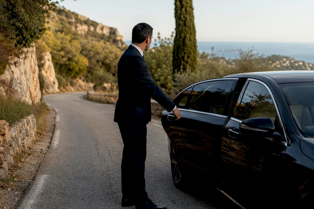 Luxury Mercedes-Benz sedan in narrow villa lane on the French Riviera with professional chauffeur opening door