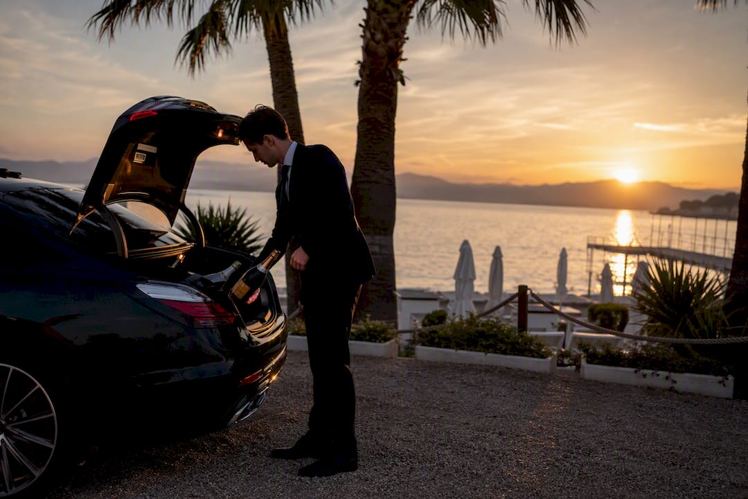 Chauffeur loading champagne at Cannes beach club sunset party with luxury car nearby