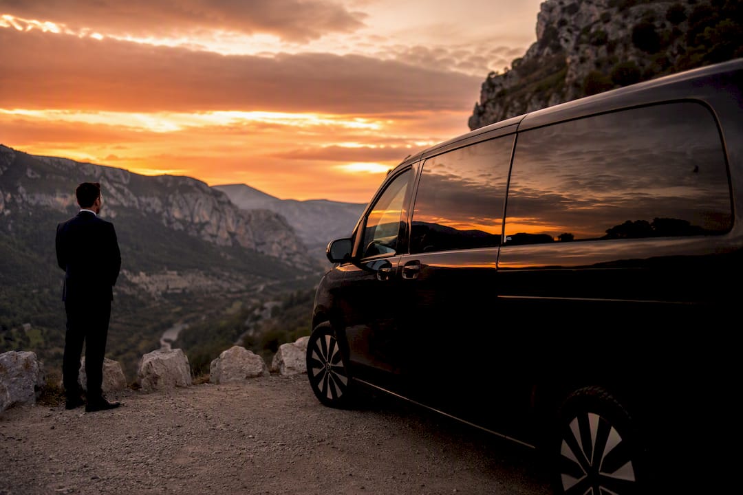 Luxury Mercedes-Benz van with chauffeur near cliff edge overlooking Gorges du Loup at sunrise