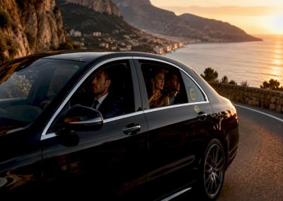 Mercedes-Benz luxury sedan chauffeured on coastal road on the French Riviera with passengers.