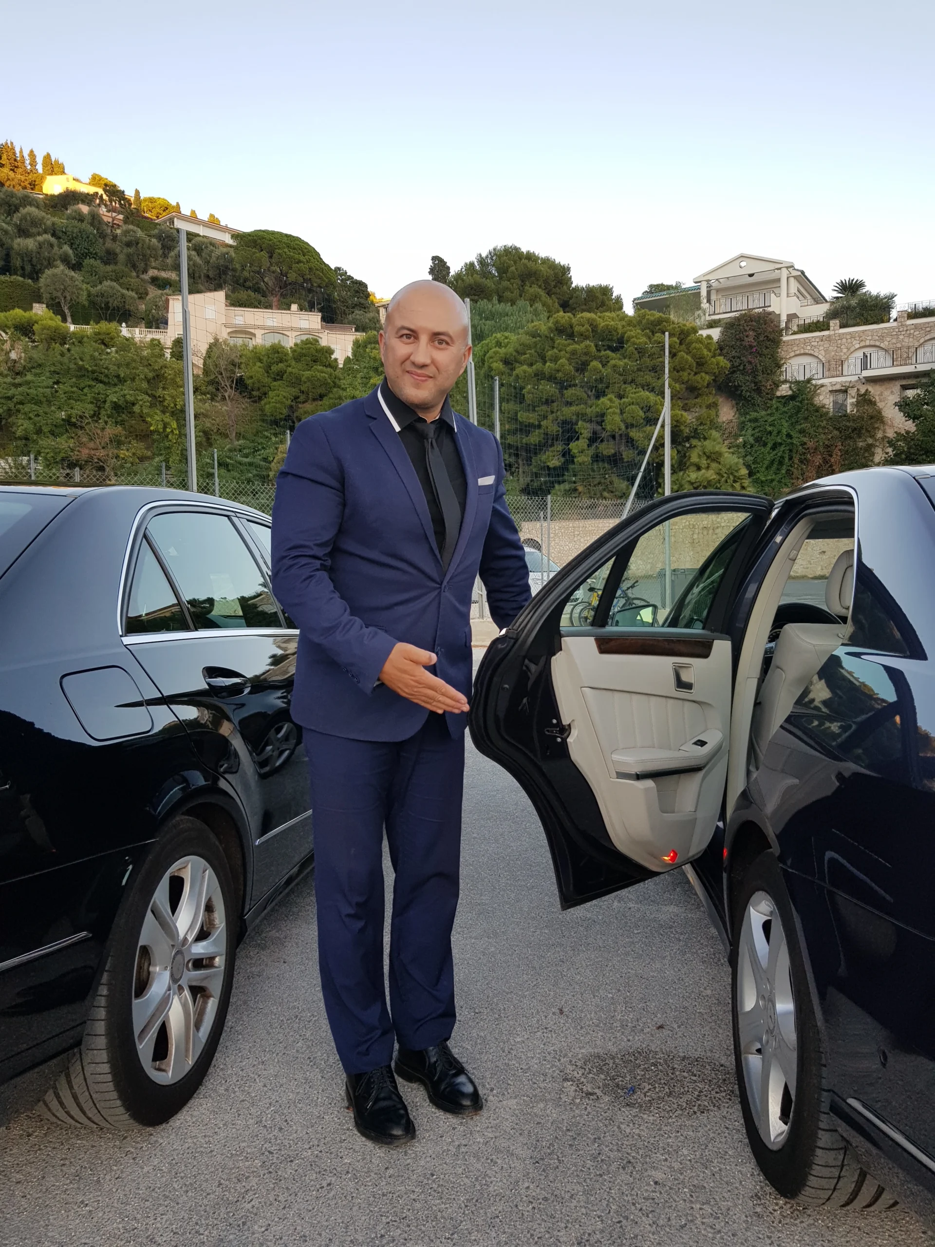 Un chauffeur TranspOnyx en costume ouvre la porte d'une Mercedes de luxe avec un geste de bienvenue pour un client VIP à Cannes.