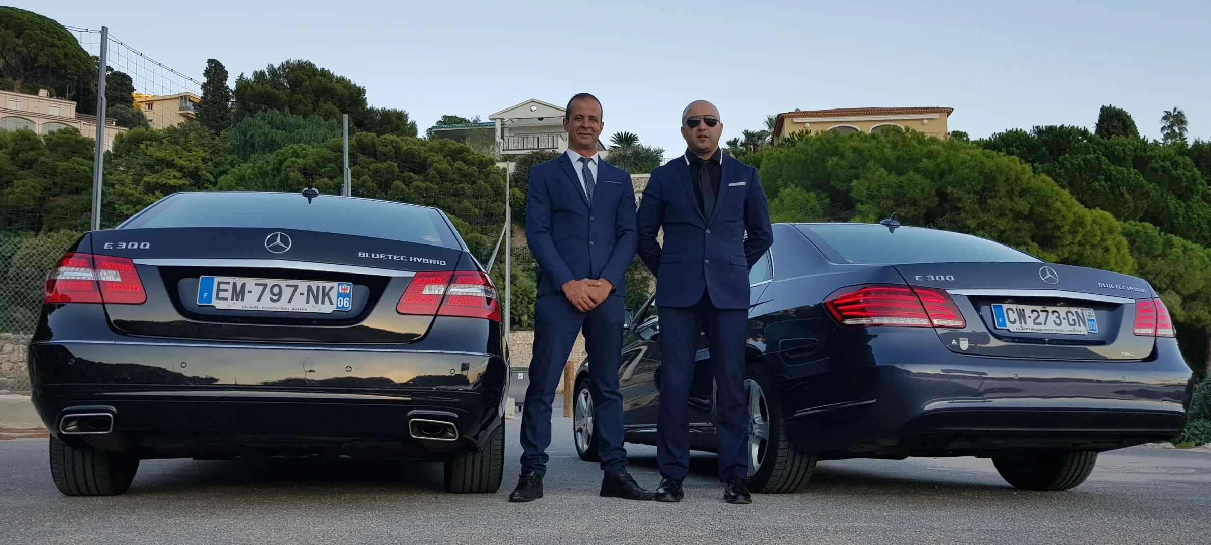 Deux chauffeurs TranspOnyx professionnels posent devant une flotte de véhicules de luxe Mercedes pour un Nice Airport Transfer vers Cannes.